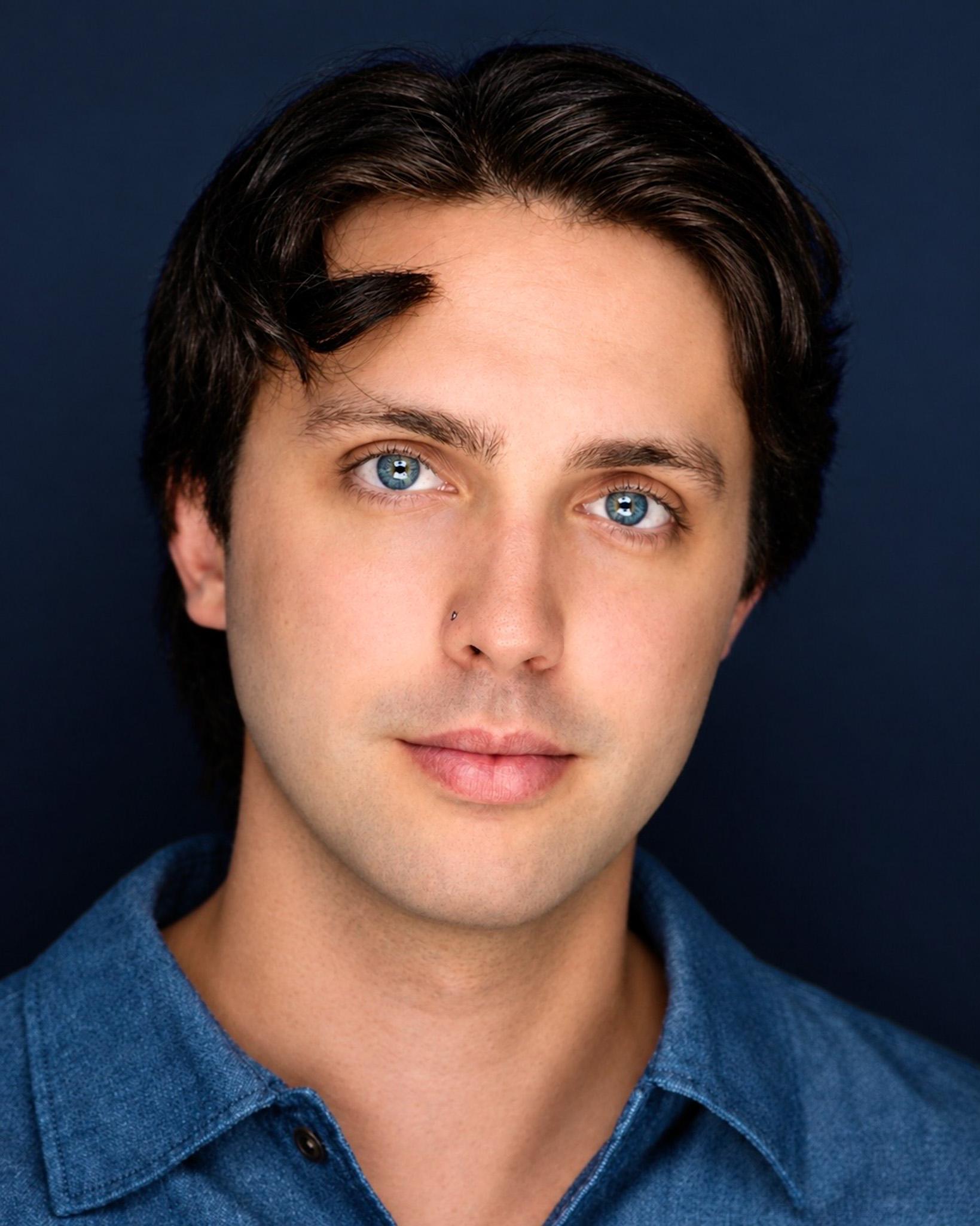 Headshot of Shane Lonergan in a blue denim shirt against a navy background